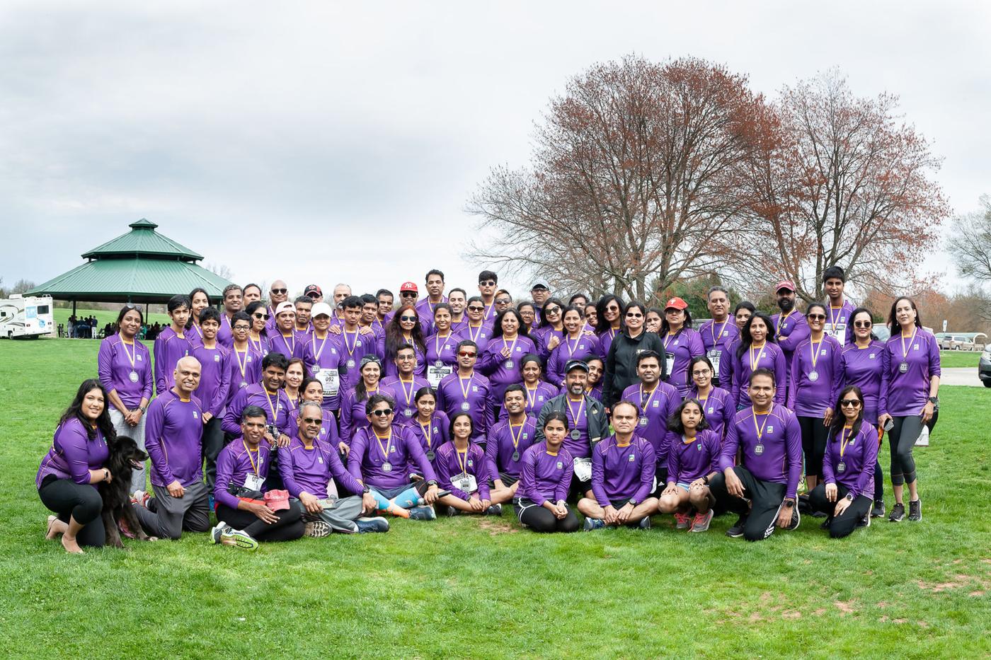 Around seventy RHWB runners in matching purple season shirts on a park lawn